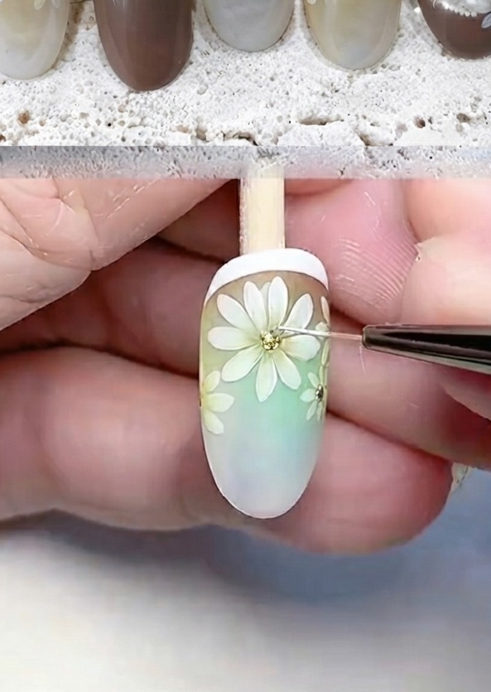 A fine tool adding glitter and white dots to the center of a painted daisy.