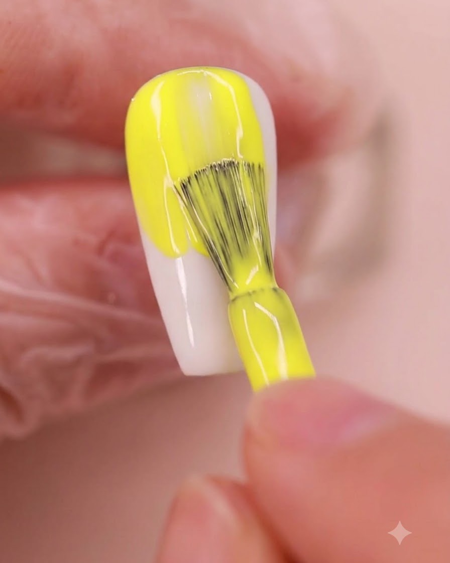 A nail brush applying a vibrant yellow gel polish evenly onto an almond-shaped nail plate.