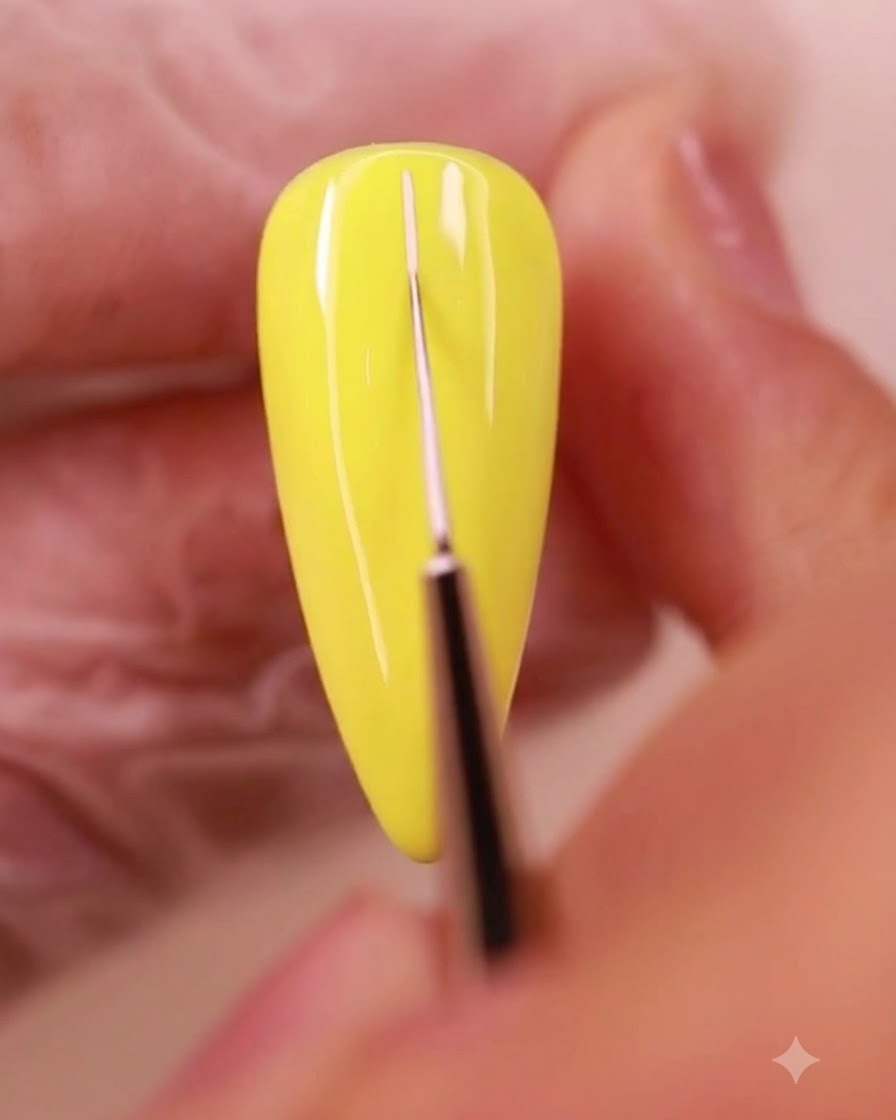 A fine liner brush drawing thin white grid lines across a yellow painted nail surface.