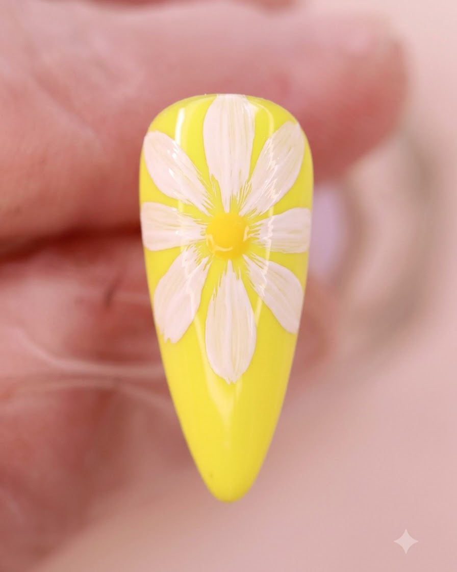A close-up view of yellow watercolor liquid blooming at the center of the white daisy petals on a yellow nail.