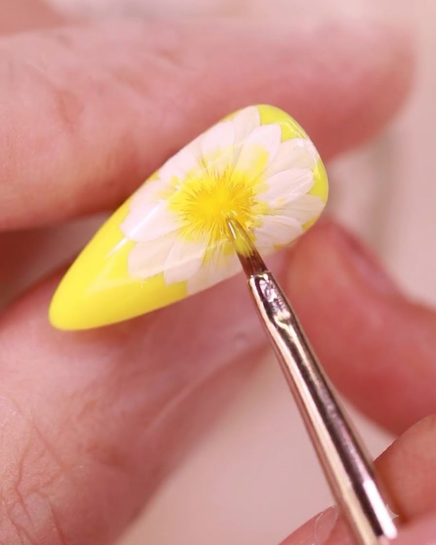 A fine detailing brush applying a clear top coat over a floral nail design.