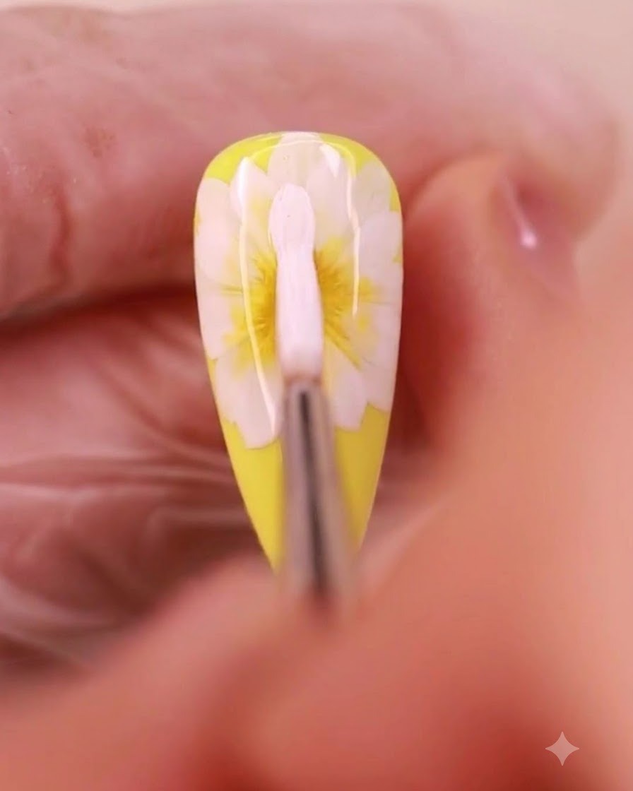 A nail art brush applying white gel to form a third layer of petals on a daisy design.