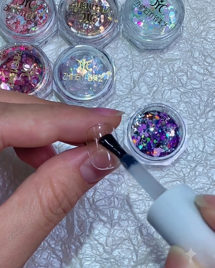 A brush holding mixed purple and silver glitter flakes over a nail covered in wet gel.