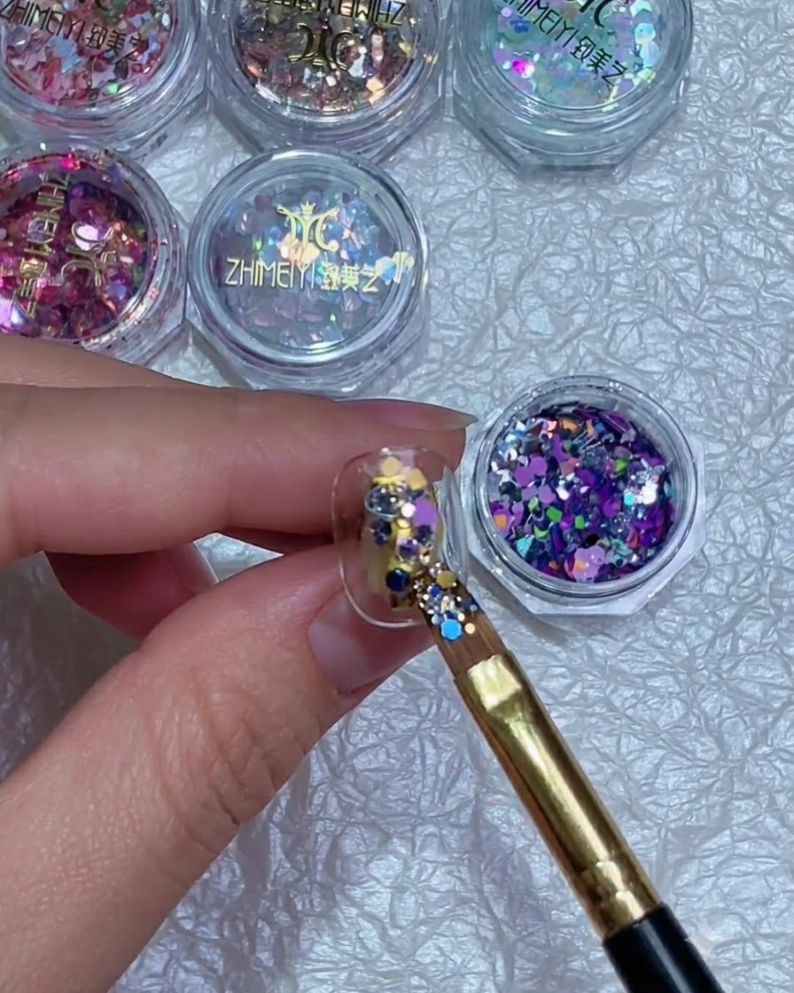 A brush precisely adjusting the position of colorful glitter flakes on a fingernail.