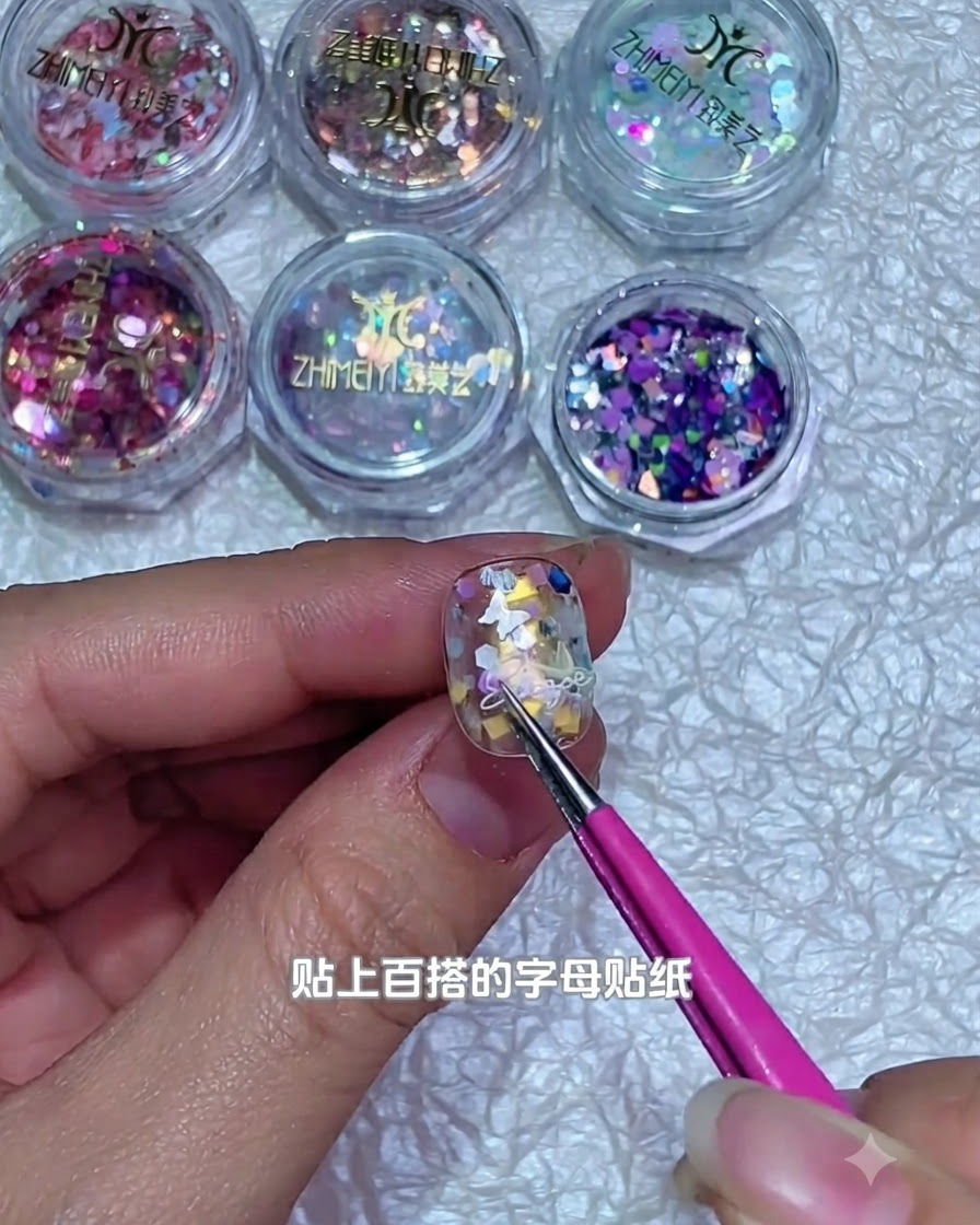 A pair of tweezers placing a tiny white letter sticker onto a decorated gel nail surface.