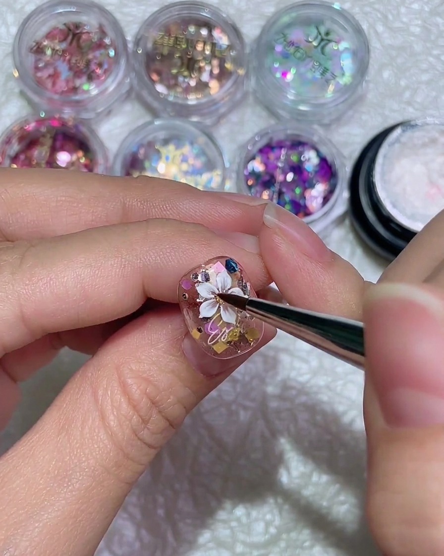 A fine liner brush drawing a single white petal for a daisy design on a glossy nail.