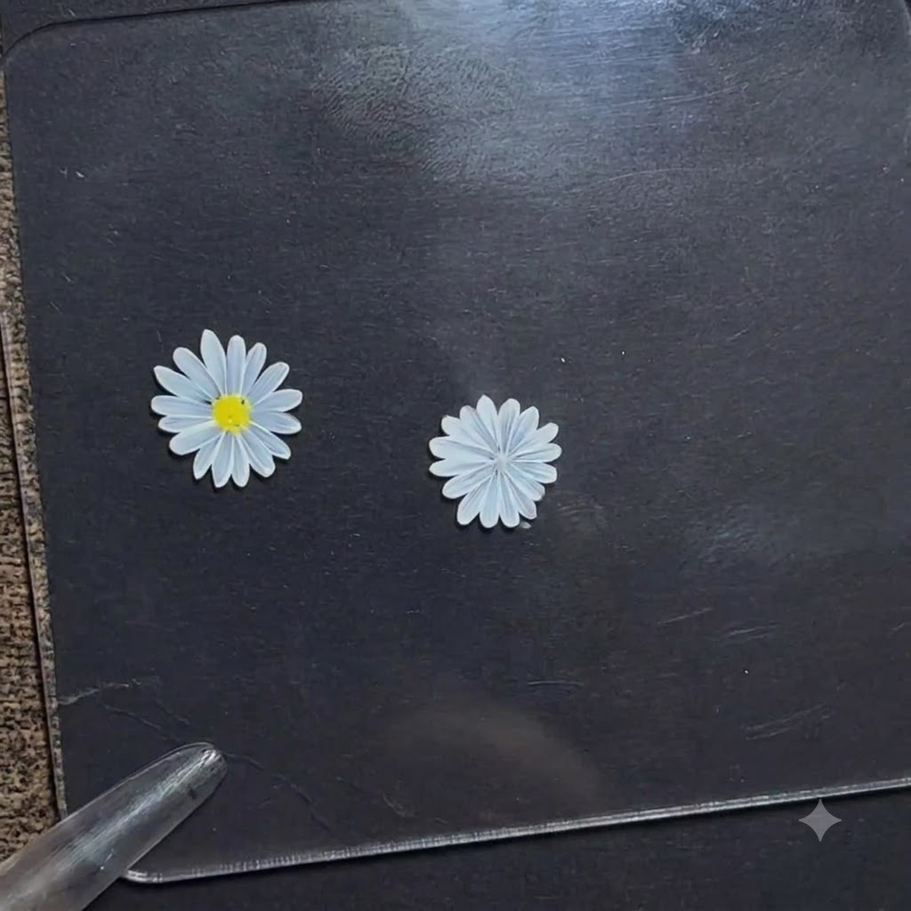 A dotting pen applying a small dot of bright yellow gel onto the center of a white daisy flower on a dark display board.
