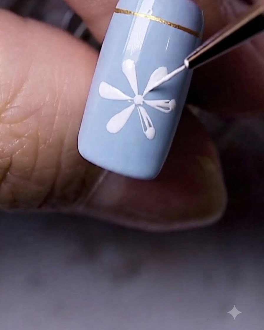 A close-up view of a completed white daisy flower painted onto a blue nail surface.