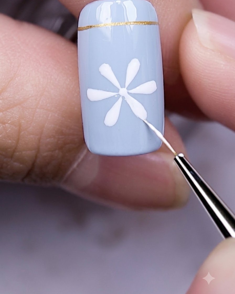 Fingers with a blue nail and white daisy art resting underneath a glowing UV LED nail lamp.