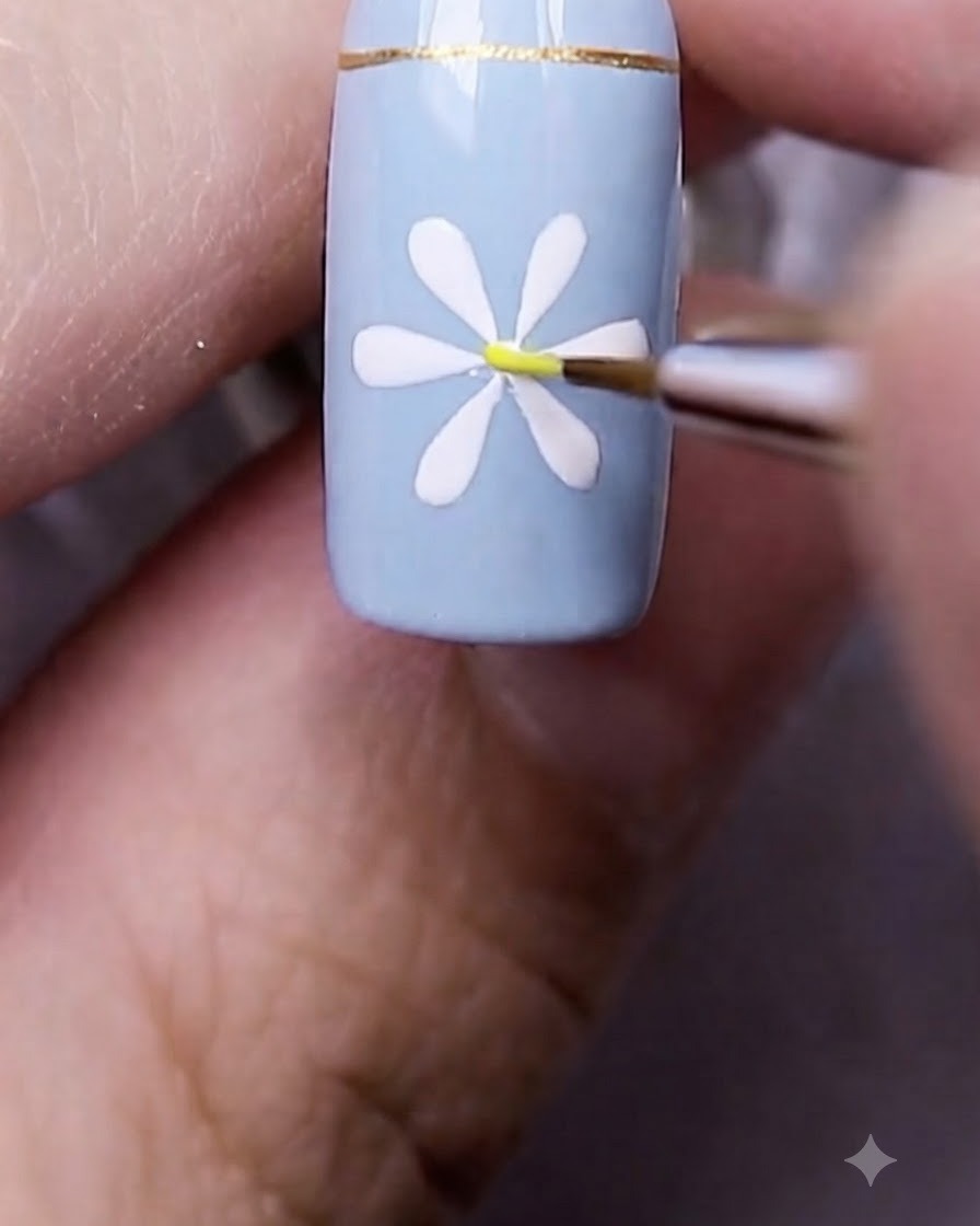 A fine nail art brush placing a tiny yellow dot directly in the center of the painted white daisy.