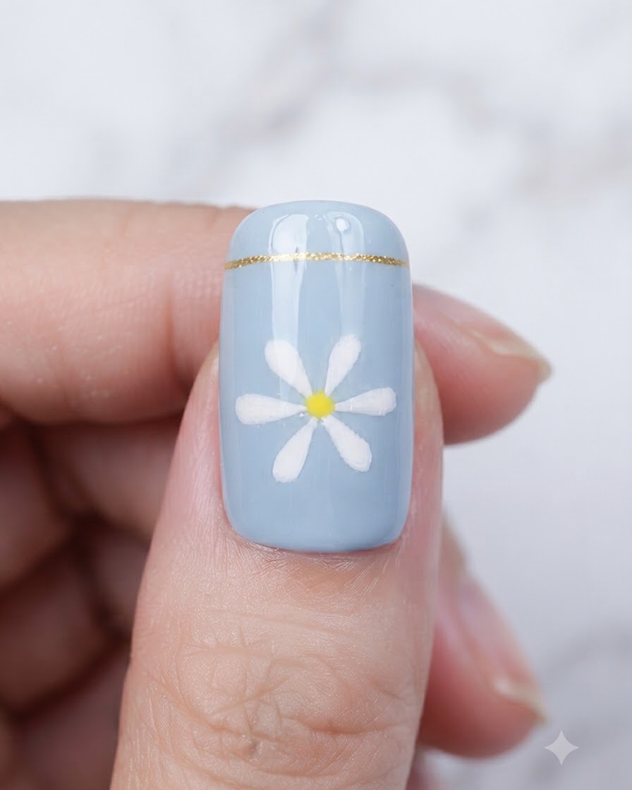 A brush applying a clear, glossy top coat over a finished blue nail with a daisy design.