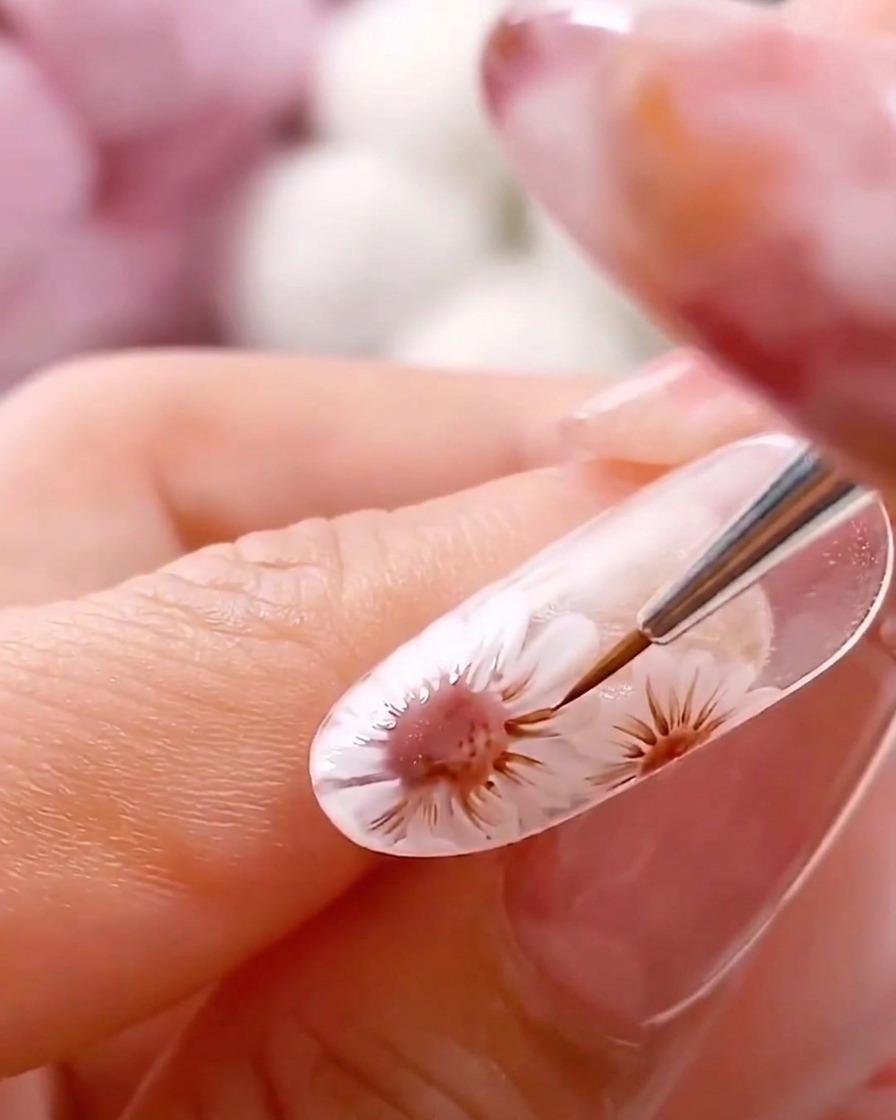 A fine liner brush pulling delicate lines outward from the brown center of the painted daisy.