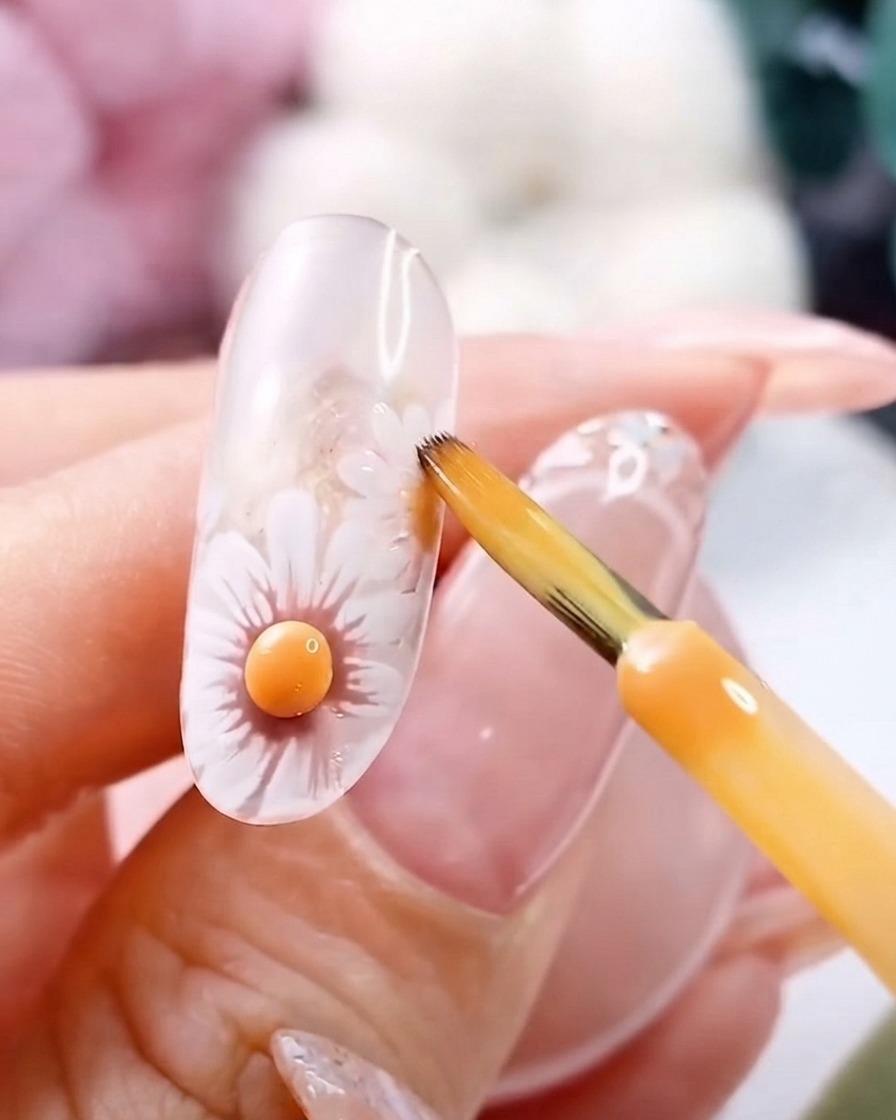 A fine brush near a cured 3D yellow flower center on a clear gel nail.