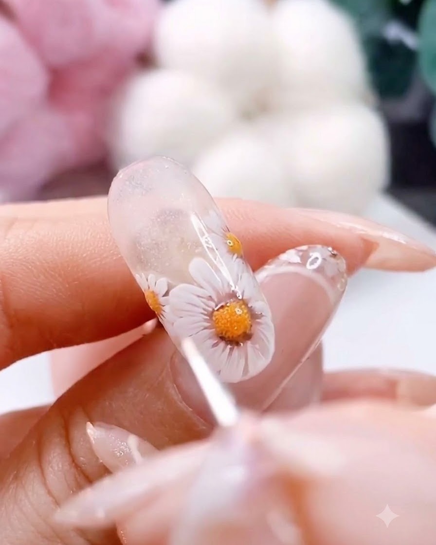 A fine detailing brush adding tiny white and brown dots around the center of a painted daisy.