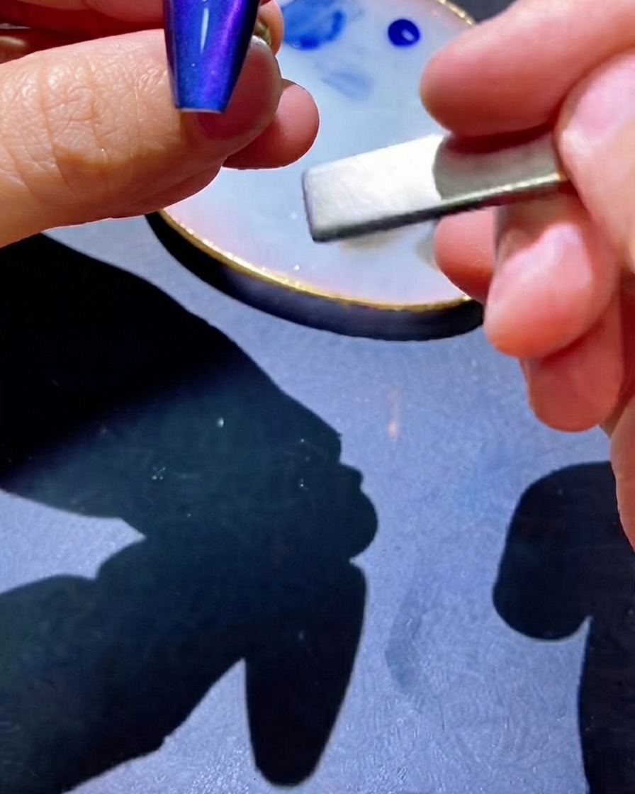 A magnet being used alongside the nail to pull pigment into a centered line.