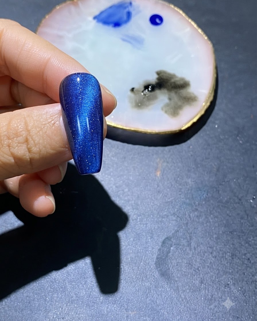 A close-up of a blue cat-eye gel nail with blue polish spots in the center and an art palette nearby.
