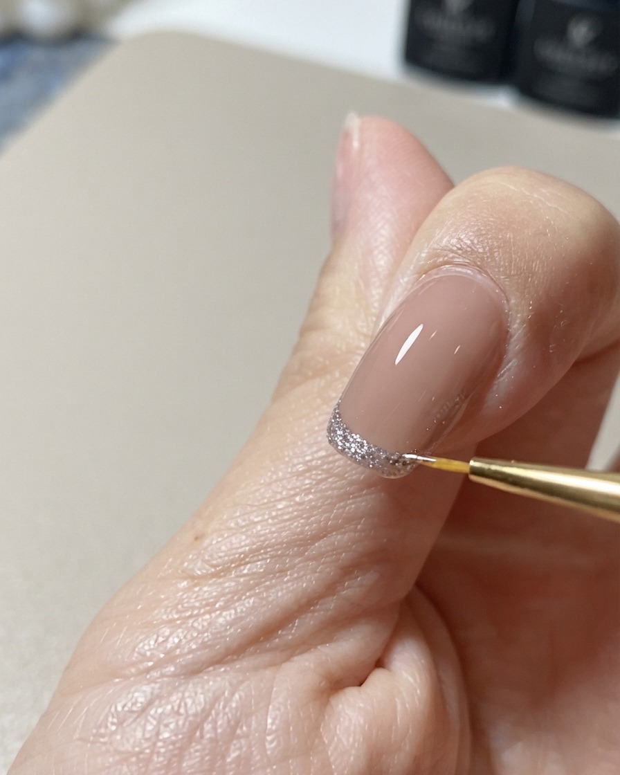 A fine nail art liner brush cleaning up and perfecting the edge of a glittering cat-eye tip design.