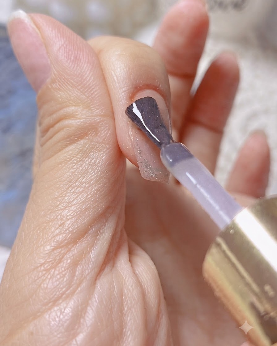 A brush applying clear builder or reinforcing gel over a shimmering cat-eye nail.
