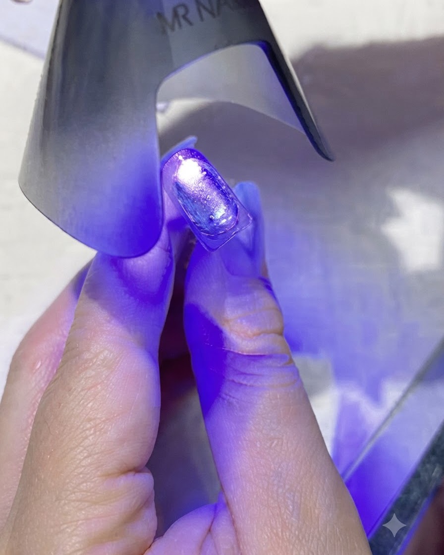 A mini purple handheld UV/LED nail lamp emitting purple light directly over a coated nail.