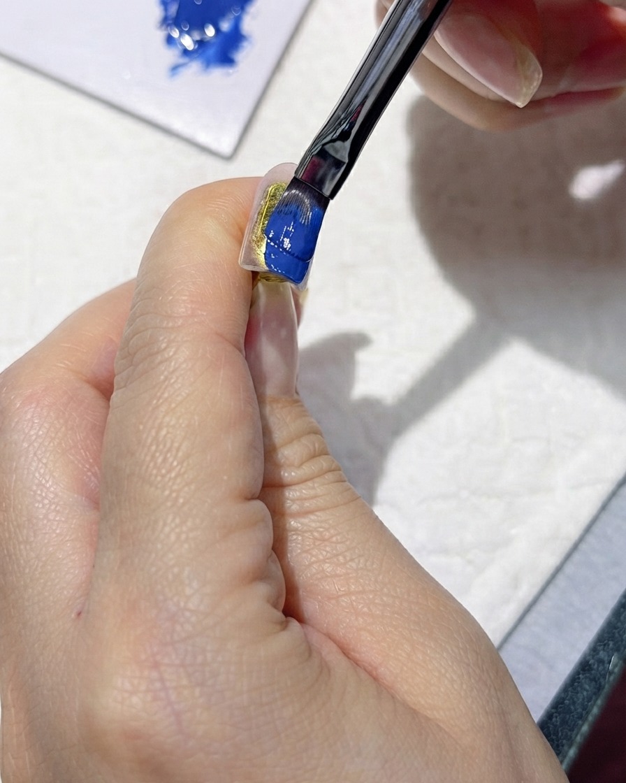 A brush carefully applying a rich dark blue gel polish onto an artificial nail.