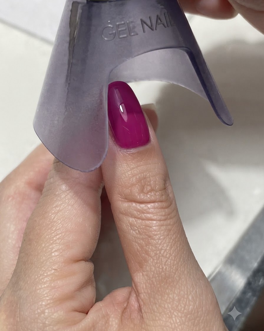 A purple handheld UV/LED lamp curing a vibrant dark magenta or blue nail under bright light.