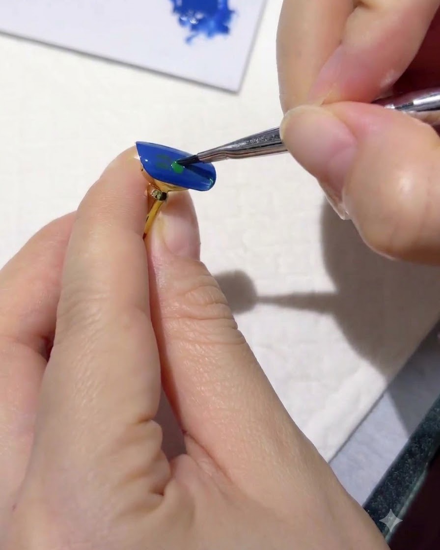 A fine liner brush adding tiny dark green leaf strokes onto a blue-painted nail surface.