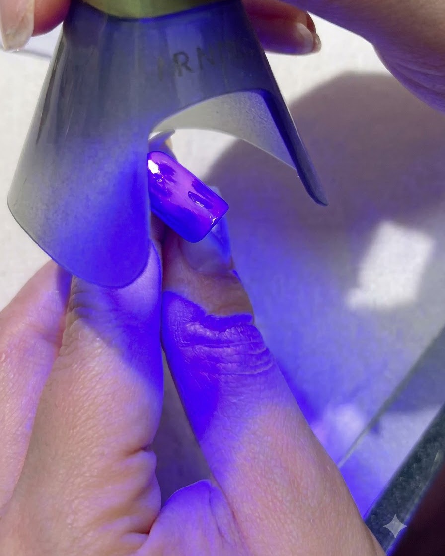 A portable purple UV lamp curing dark green leaf nail art on a blue-painted fingernail.