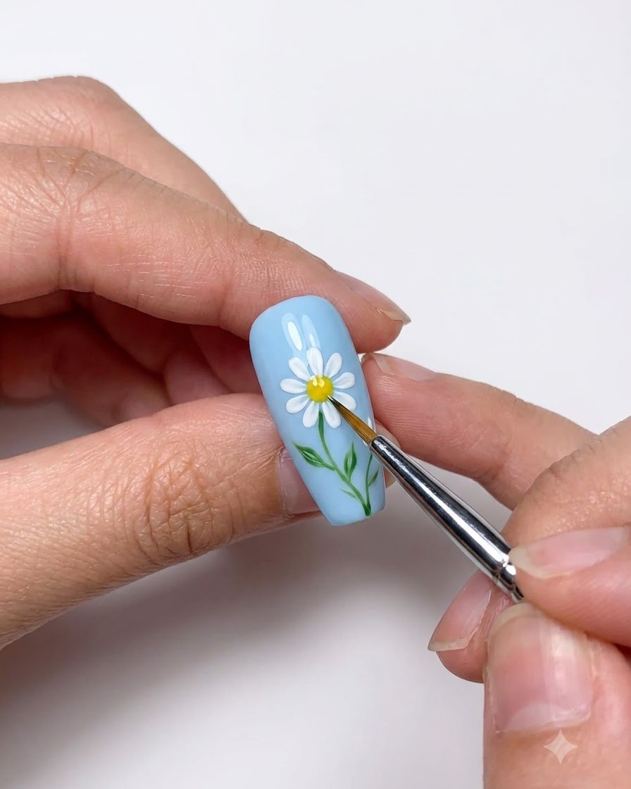 A close-up of a dotting tool placing a yellow center onto the painted white daisy.