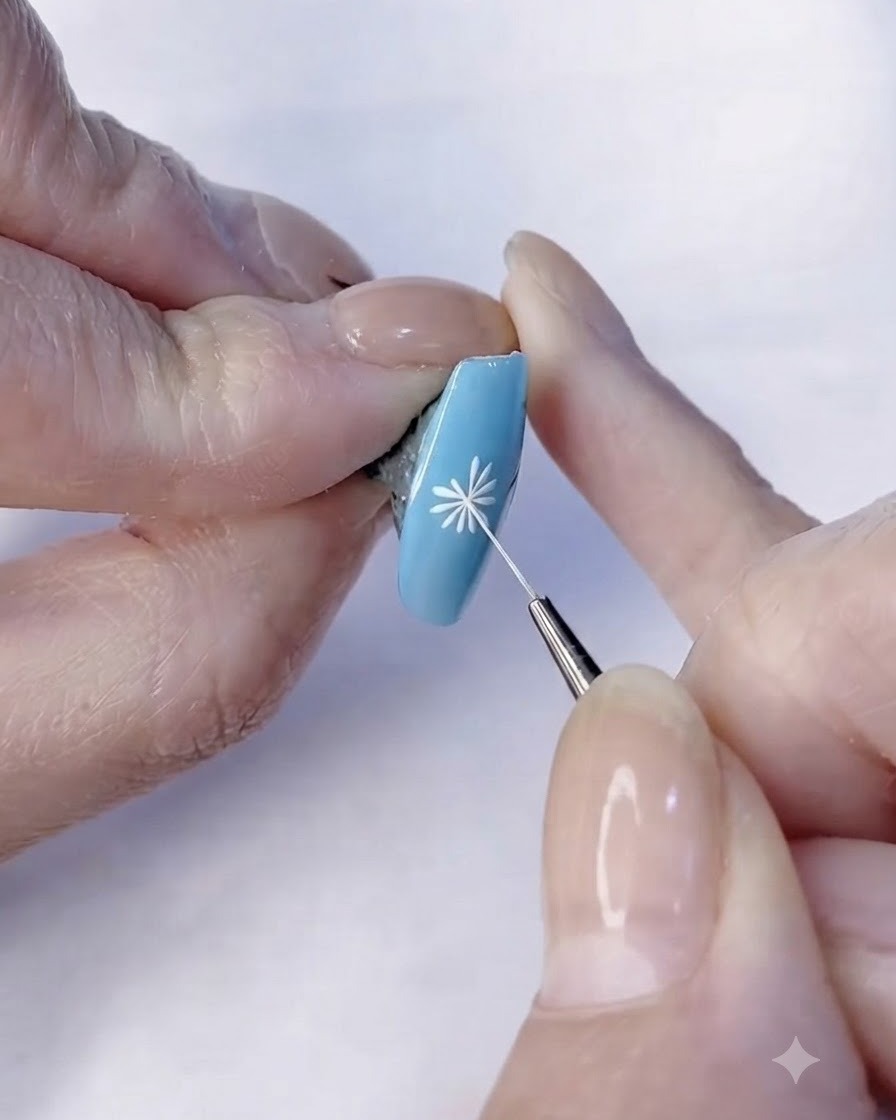 A fine brush finishing the white petal details of a daisy nail art design.