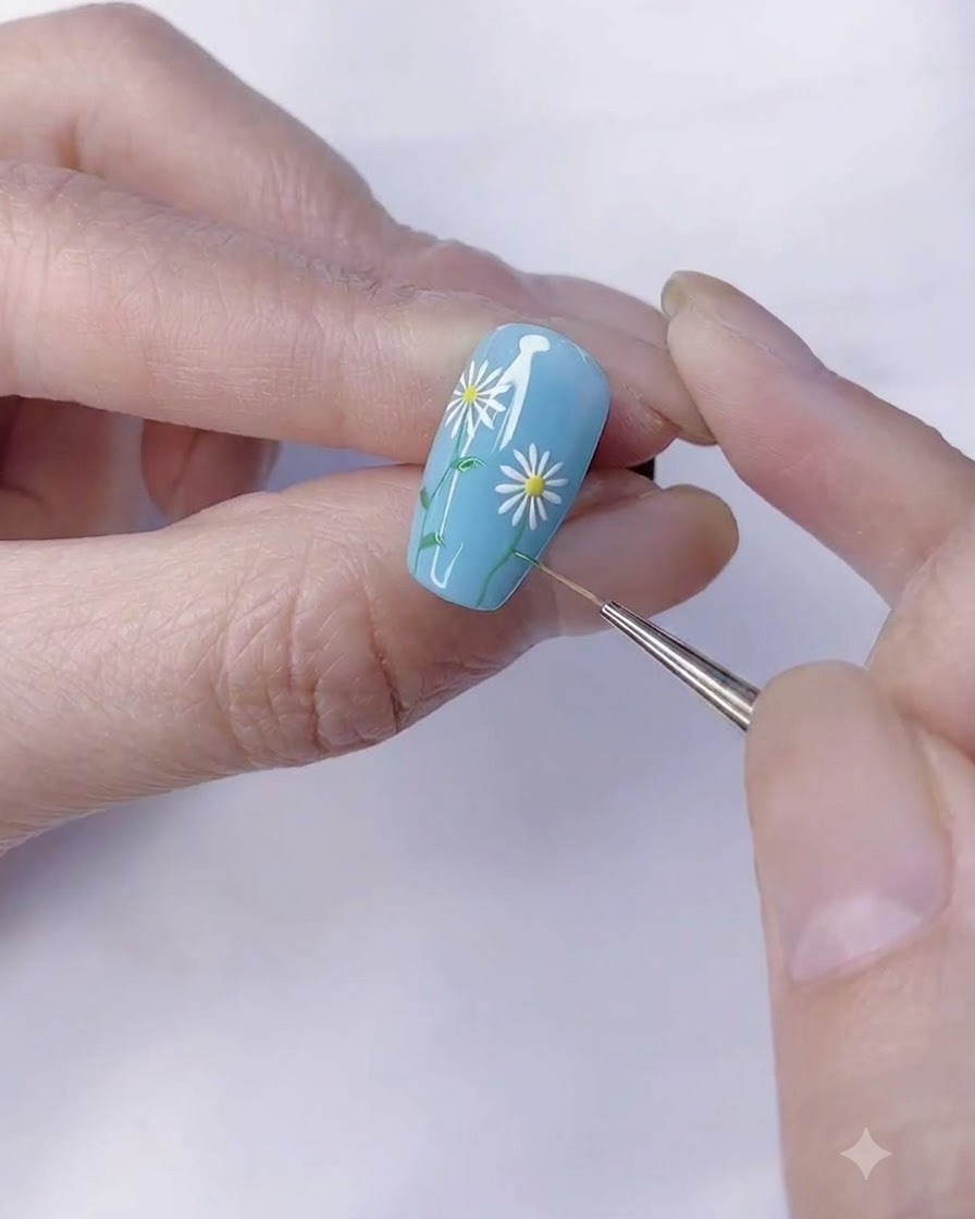 A fine detail brush adding small green leaves to the daisy stem.