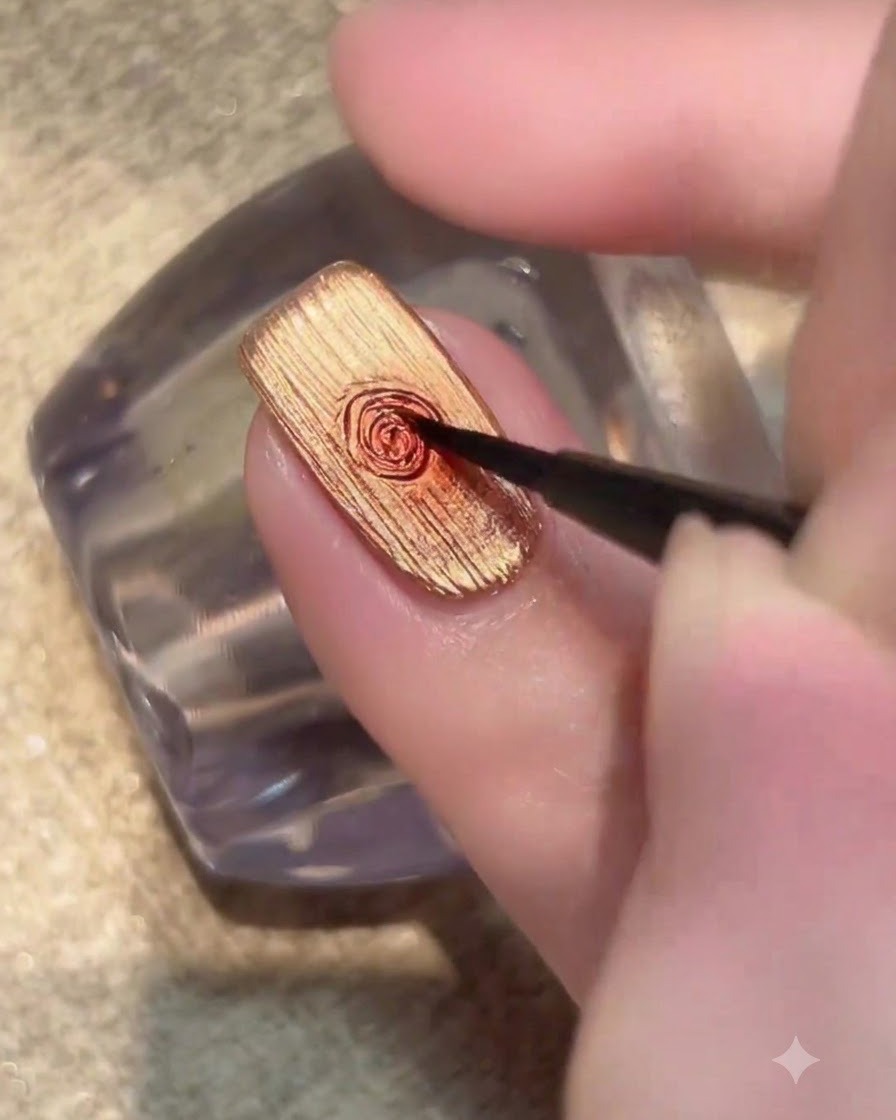 A fine brush placing a small dot of dark red gel in the middle of a gold nail.