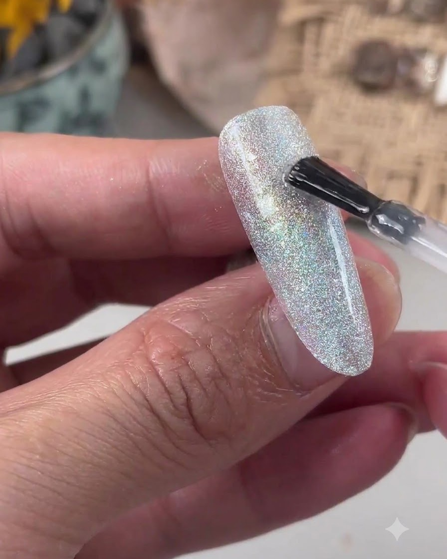 A brush applying clear leveling gel onto a glittery nail surface.