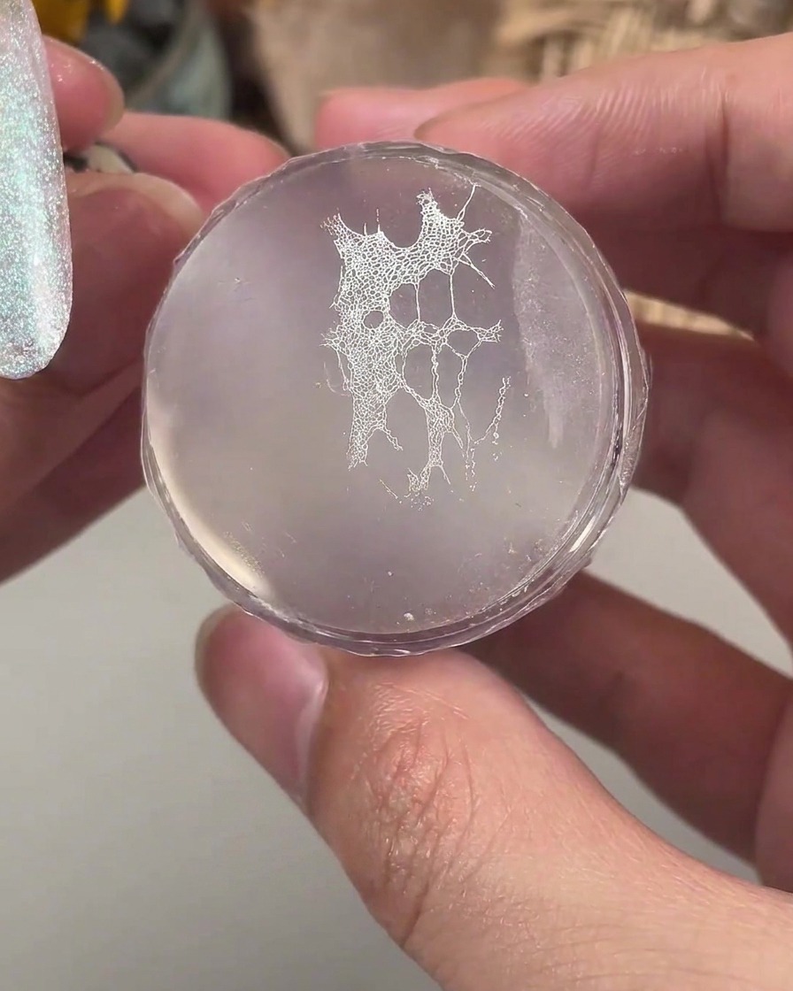 A clear silicone stamper holding a fine white lace pattern ready to be transferred onto a manicured nail.
