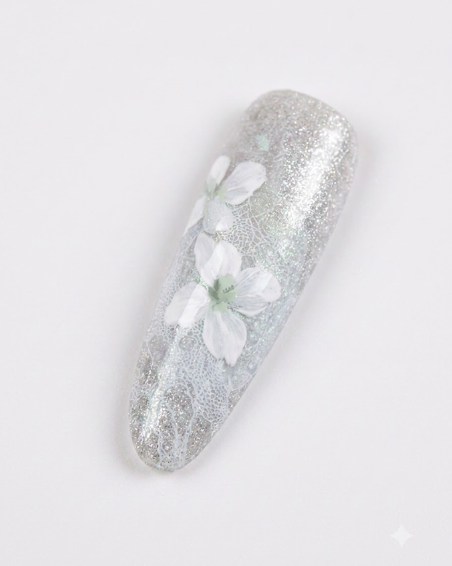 A close-up of a manicured nail featuring delicate white flowers with soft grey shading over a sparkling grey-blue background.
