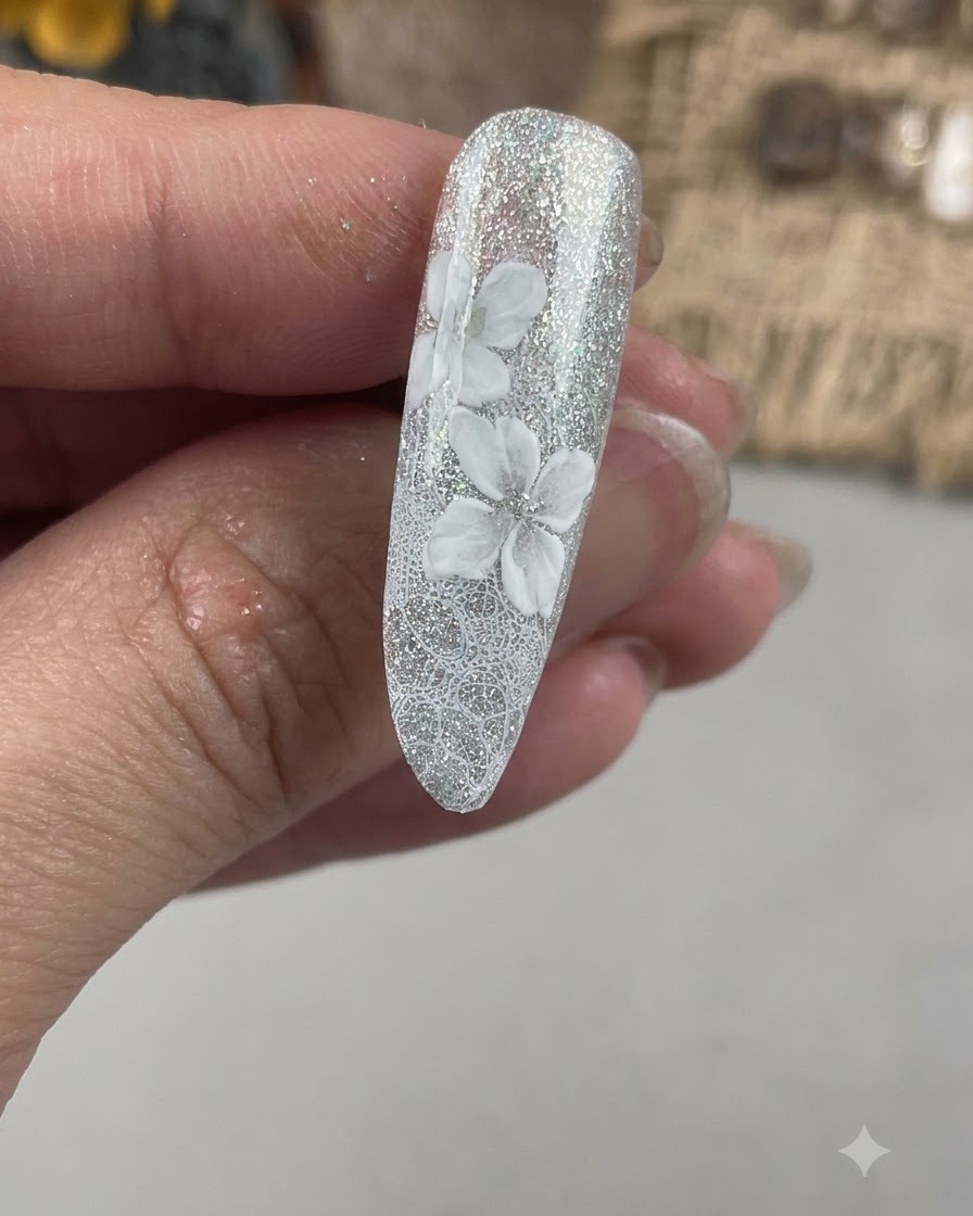 A close-up of a fingernail showing a second layer of white petals being painted offset from the initial flower base.