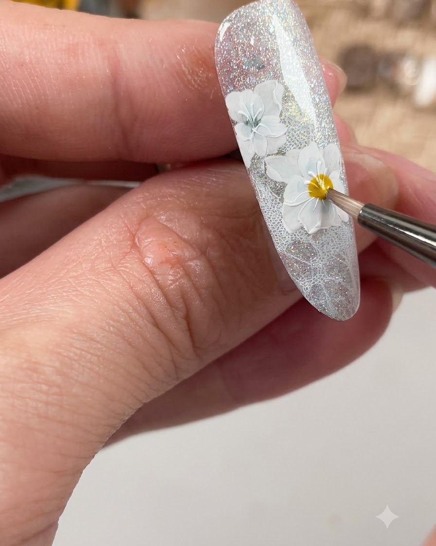 A nail brush applying a matte top coat specifically over the crafted white flower details on the nail.