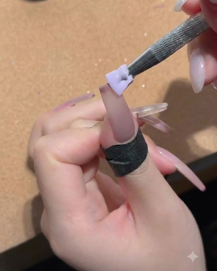 A small sponge held by a metal tool dabbing peach nude gel onto the nail surface.