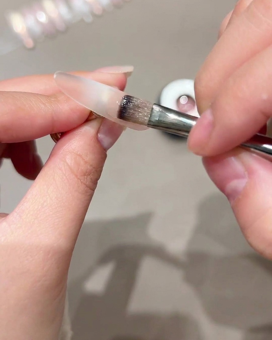 A brush applying cat-eye gel onto the outer portion of a clear nail tip.