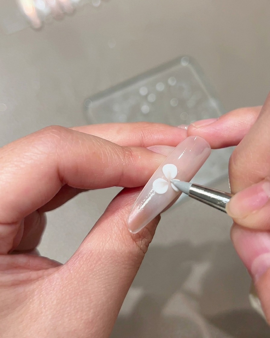 A silicone sculpting brush pressing and shaping a white gel petal on a nude manicured nail.