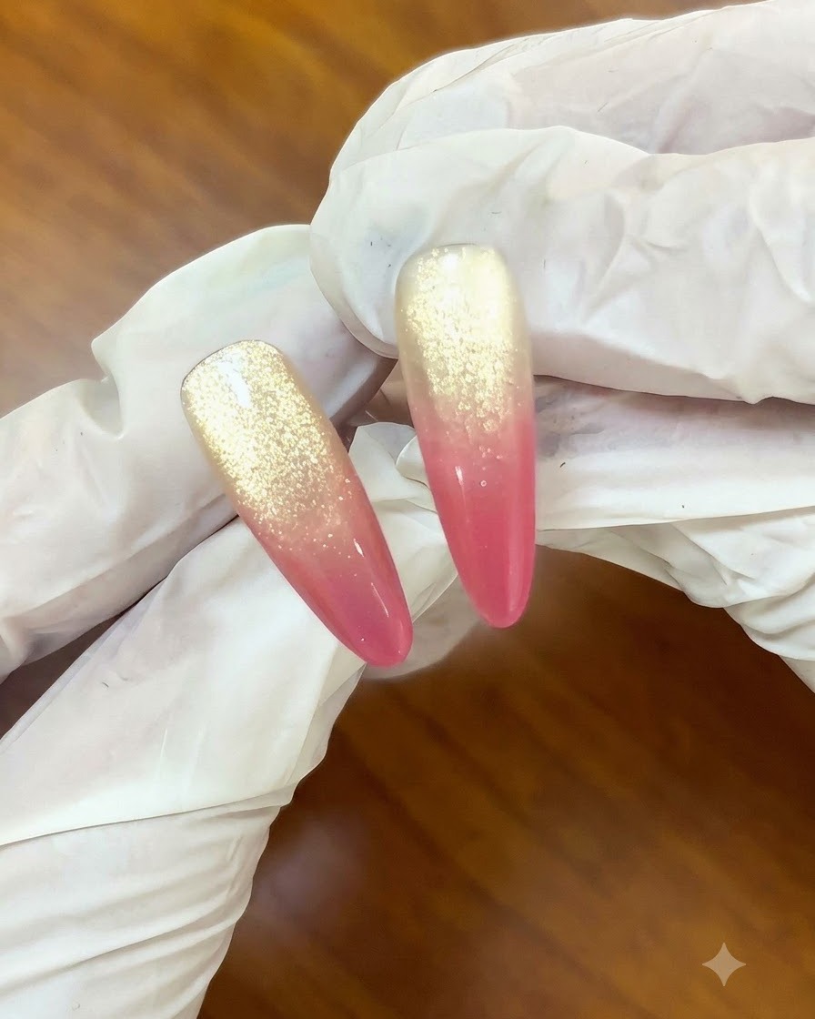 A brush applying a clear top coat over a sunset rose and gold cat-eye gradient nail design.