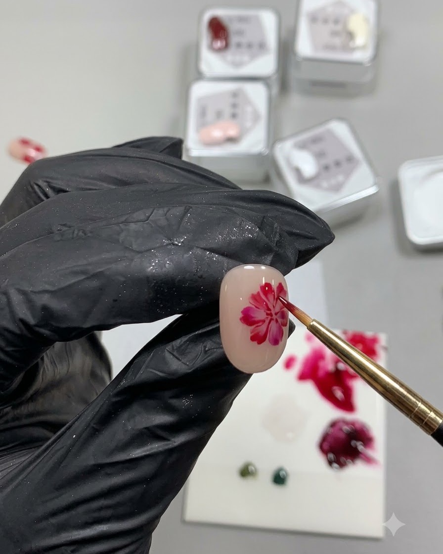 A fine detail brush painting a soft, translucent, irregular red circle resembling a rose petal base on a nude nail.