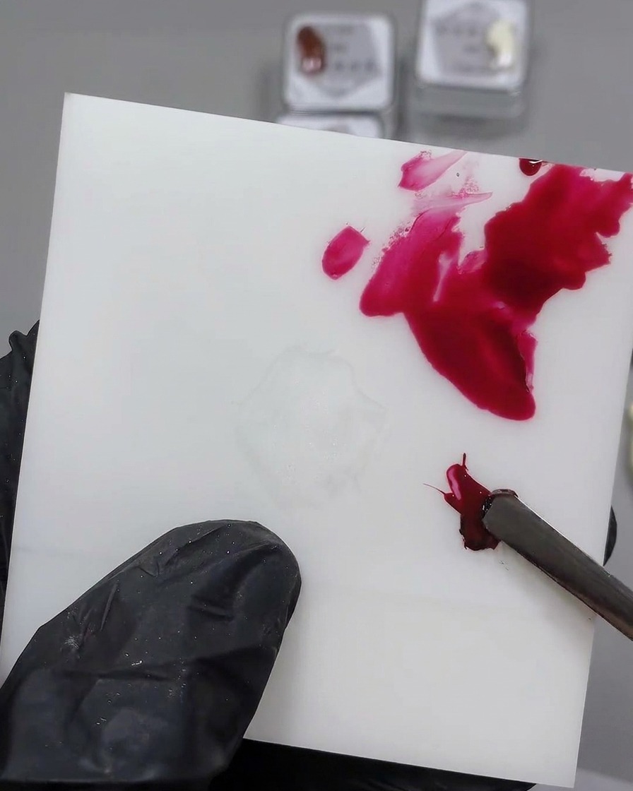 A metal tool mixing black gel into a red gel dollop on a white palette.