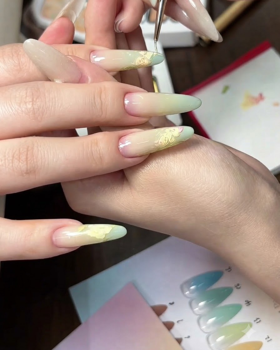 A close-up view of applying a light green gel gradient onto the tips of oval-shaped nails using a sponge.