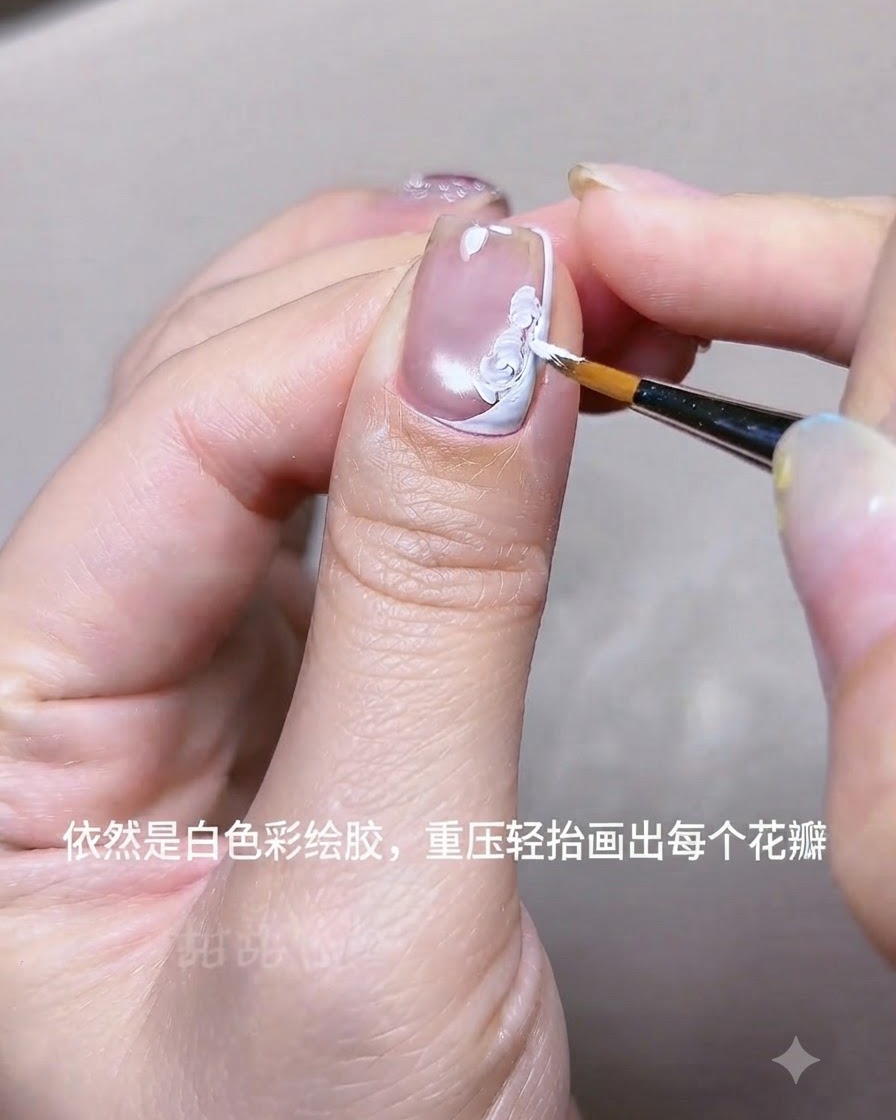 A close-up view of a hand using a fine liner brush to paint white acrylic gel flower petals on a nail near a white French tip line.