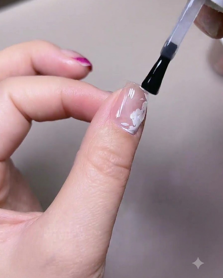 A brush applying a coat of matte top gel polish over a nail with pre-painted white rose elements.
