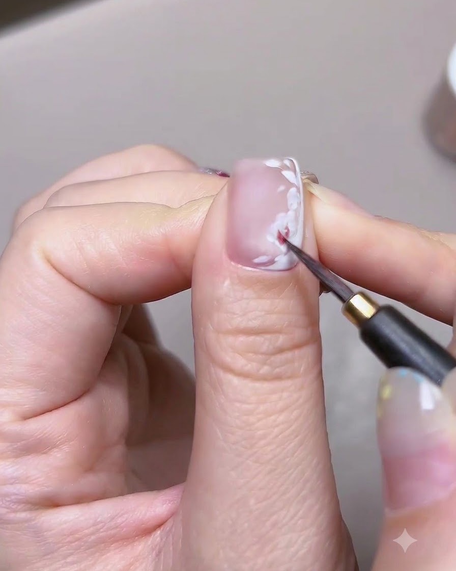 A detailed close-up of a fine brush applying red watercolor paint onto the white petal base of a nail art rose.