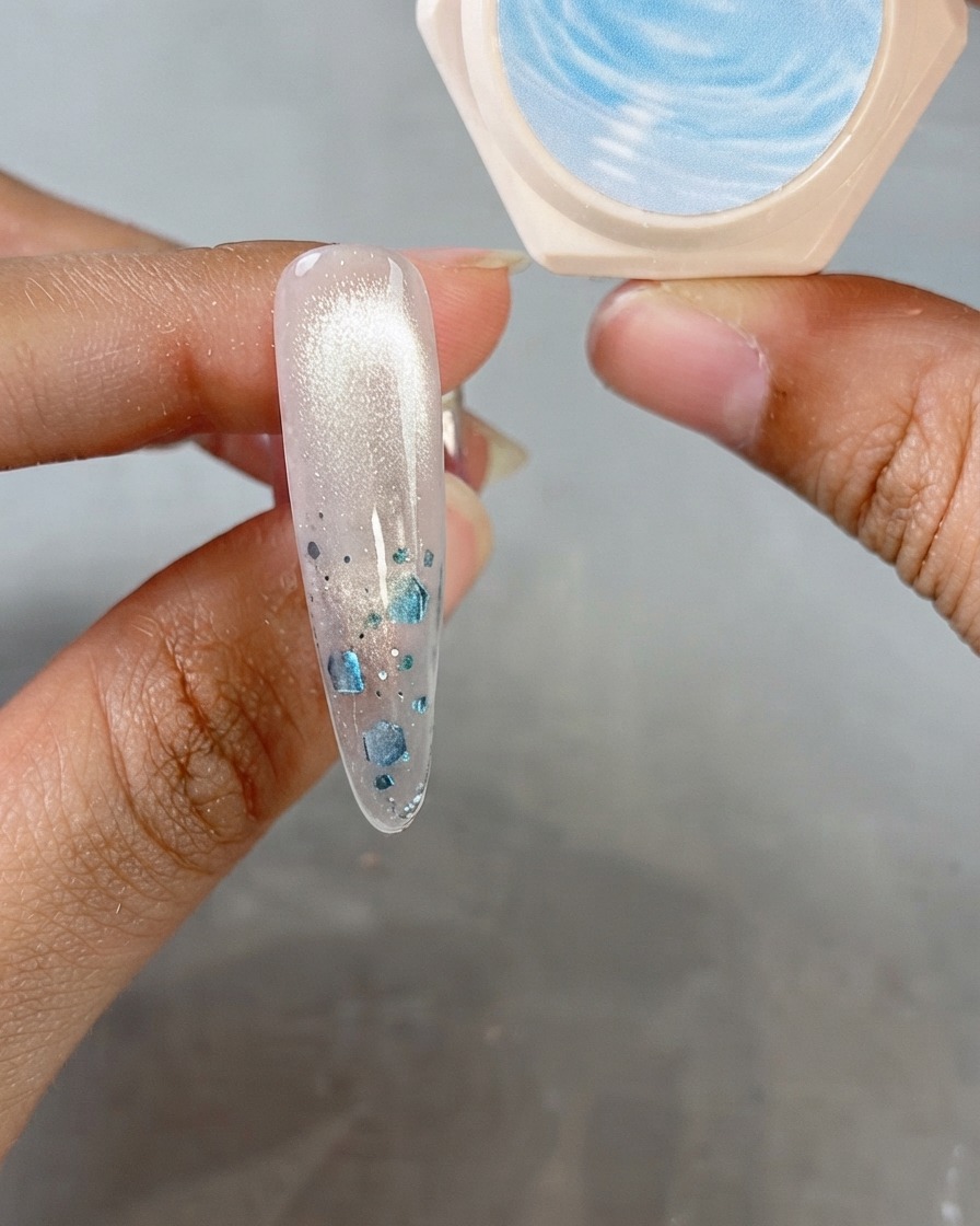 An almond nail showing a shimmering cat-eye finish with a jar of crystal gel in the background.