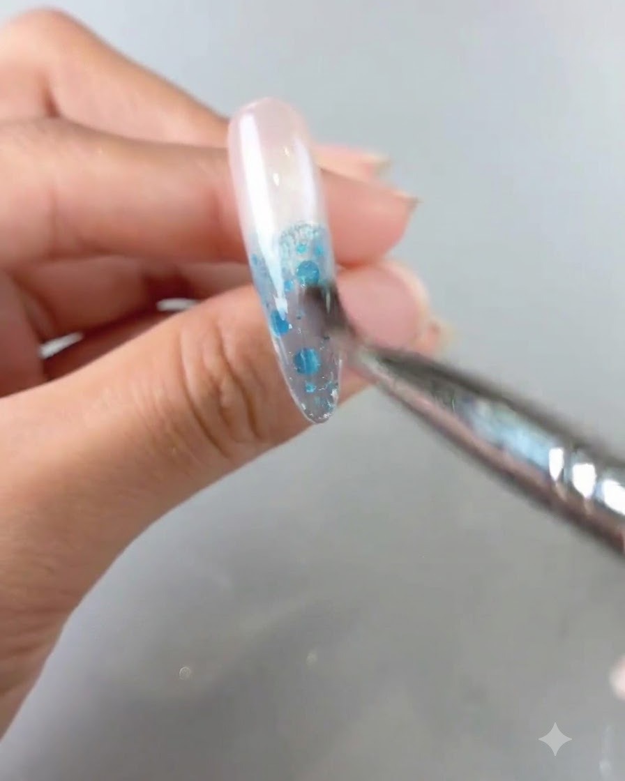 A close-up view of a brush blending blue gel product on a nail to create an ombre gradient.