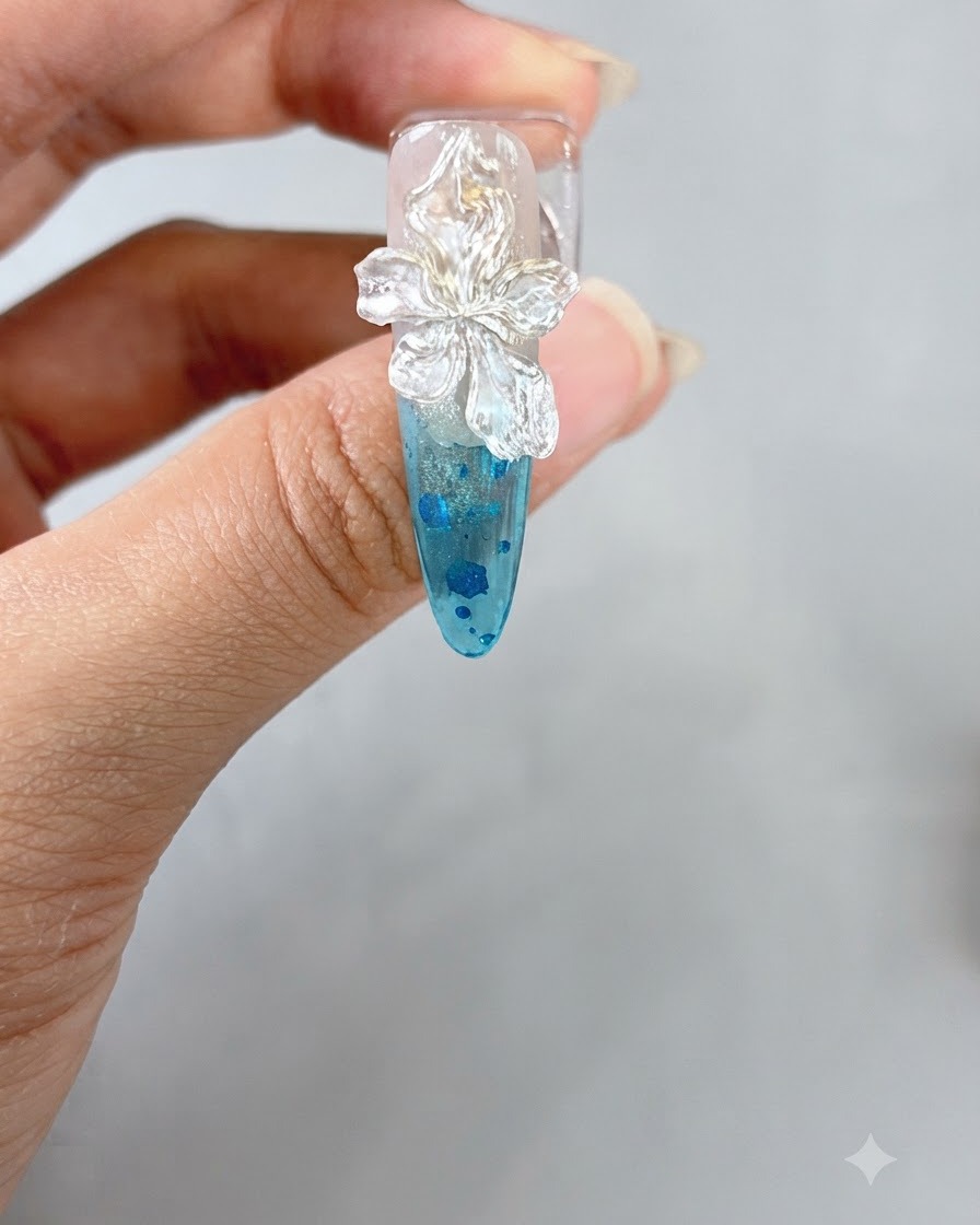 A pair of tweezers placing a small white pearl onto the center of a sculpted 3D flower on a nail.