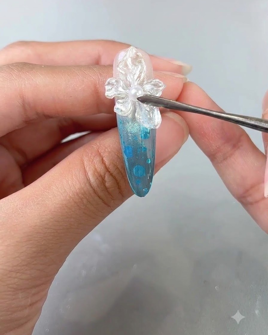 A close-up of a manicured finger receiving a final clear top coat application over a textured flower nail art design.
